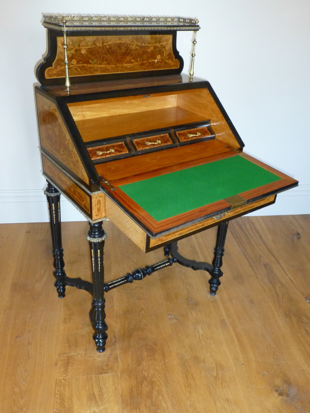 A nineteenth-century French slope-front writing desk featuring floral amboyna marquetry, ebonised turned legs with a shaped stretcher, and a brass gallery rail top. View VIII