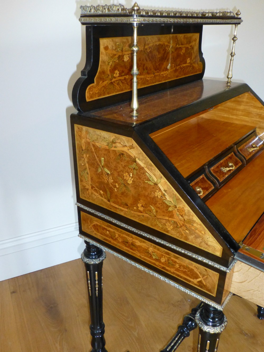A nineteenth-century French slope-front writing desk featuring floral amboyna marquetry, ebonised turned legs with a shaped stretcher, and a brass gallery rail top. View IX