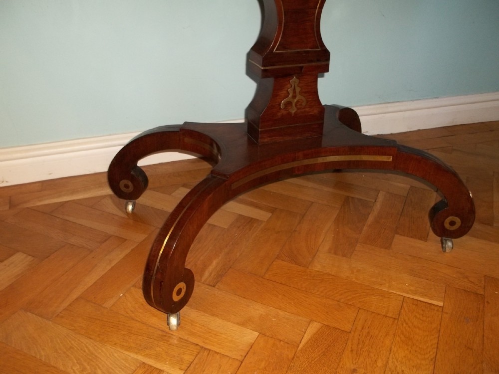 A Regency rosewood sofa table featuring drop leaves, brass inlay stringing, a central square pedestal, and splayed quadruped legs on castors. View VI