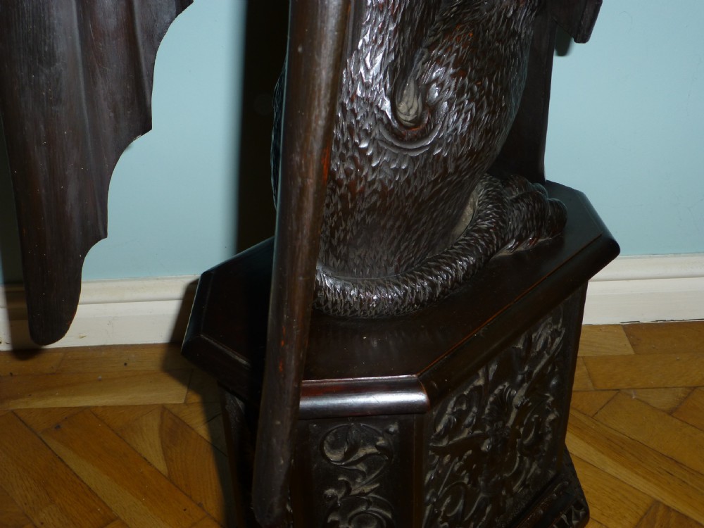 A dark carved wooden torchere stand featuring a detailed winged griffin holding a shield on an octagonal plinth base supporting an octagonal top. View VII