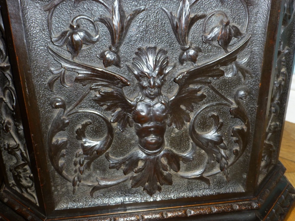 A dark carved wooden torchere stand featuring a detailed winged griffin holding a shield on an octagonal plinth base supporting an octagonal top. View VIII