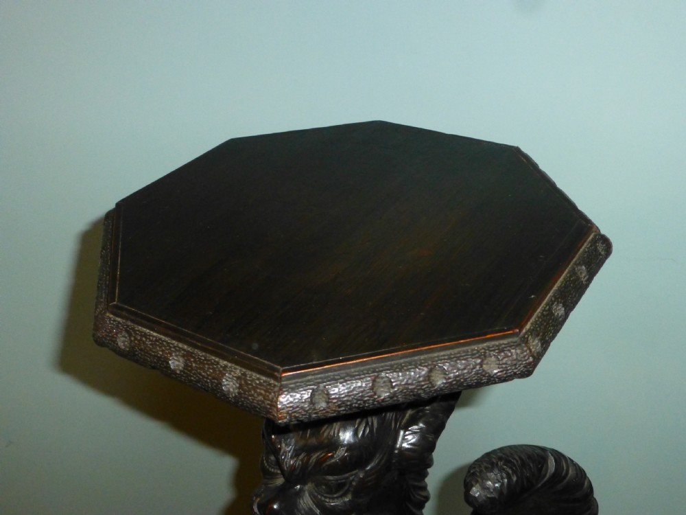 A dark carved wooden torchere stand featuring a detailed winged griffin holding a shield on an octagonal plinth base supporting an octagonal top. View XI