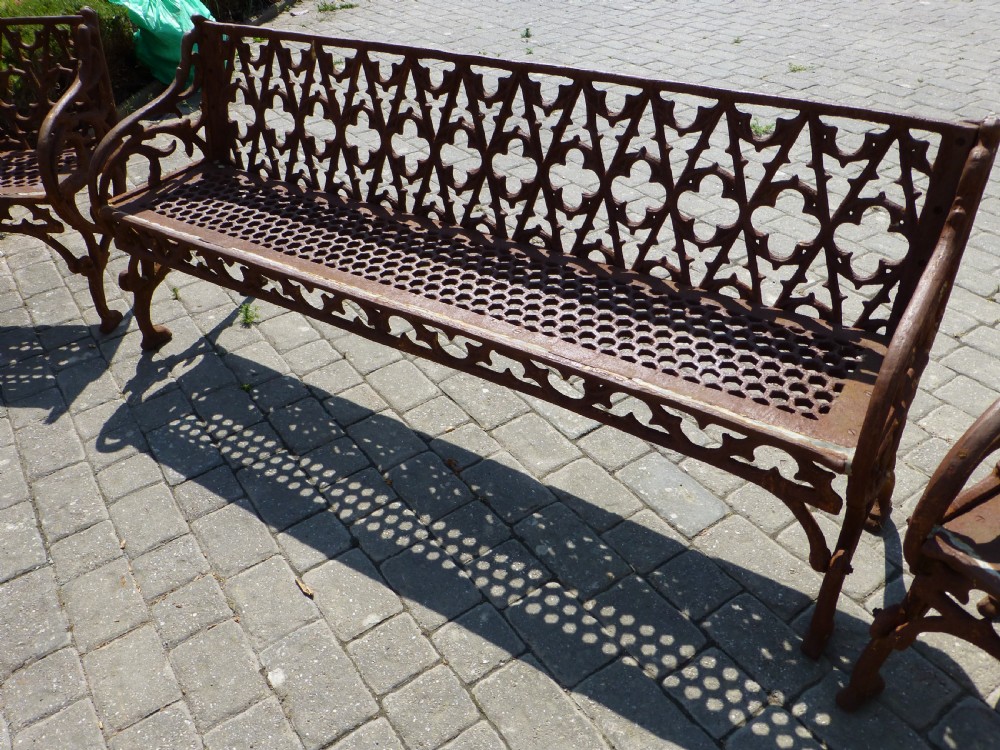 A three-piece antique cast iron garden set comprising a wide bench and two matching armchairs featuring openwork Gothic tracery backrests and weathered brown surface oxidisation. View II
