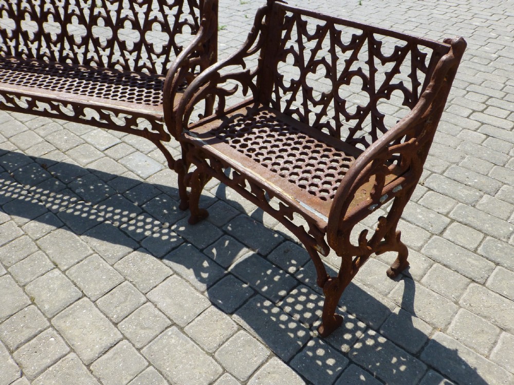 A three-piece antique cast iron garden set comprising a wide bench and two matching armchairs featuring openwork Gothic tracery backrests and weathered brown surface oxidisation. View III
