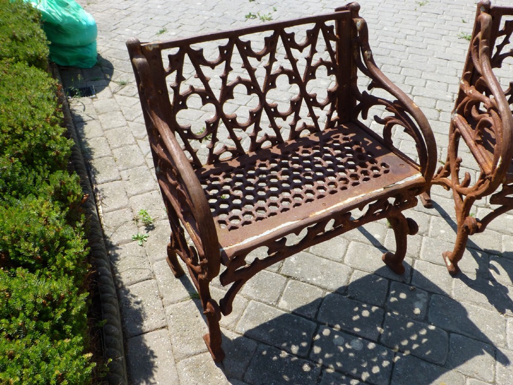 A three-piece antique cast iron garden set comprising a wide bench and two matching armchairs featuring openwork Gothic tracery backrests and weathered brown surface oxidisation. View IV