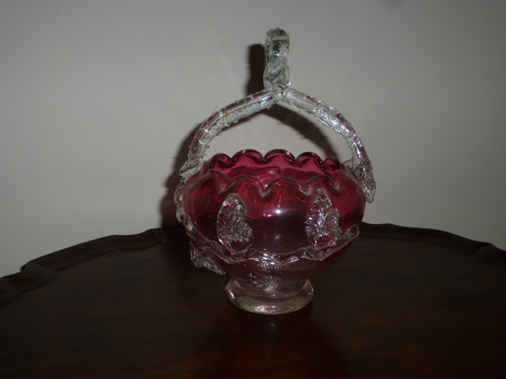 A nineteenth-century Victorian hand-blown cranberry glass bonbon dish with a crimped rim, clear glass overhead handle, and applied glass leaf accents.