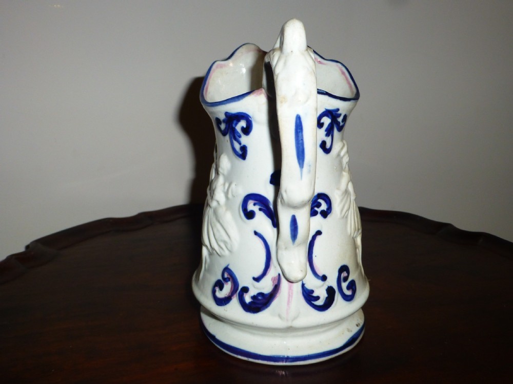 A white ceramic Staffordshire milk jug featuring raised relief mouldings and hand-painted cobalt blue scroll accents.