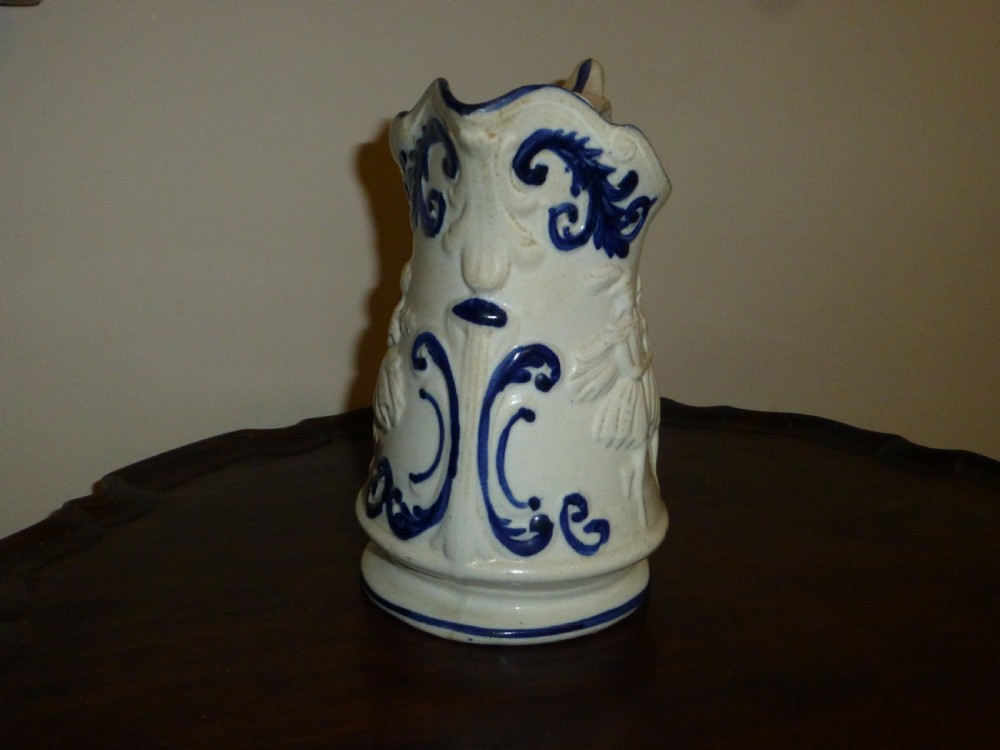 A white ceramic Staffordshire milk jug featuring raised relief mouldings and hand-painted cobalt blue scroll accents. View III