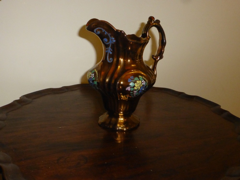 An antique copper lustre ceramic milk jug featuring hand-painted floral enamel details on a fluted body with a sculpted handle.