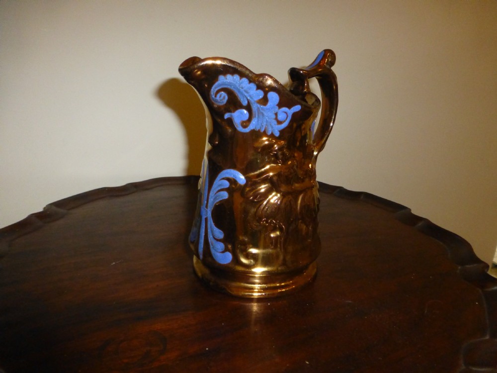 A Victorian Staffordshire earthenware jug featuring a reflective copper lustre glaze, moulded relief figures, blue floral scroll decoration, and a shaped handle.