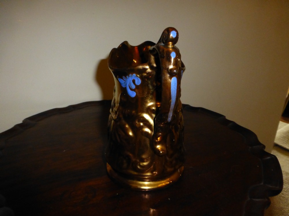 A Victorian Staffordshire earthenware jug featuring a reflective copper lustre glaze, moulded relief figures, blue floral scroll decoration, and a shaped handle. View III
