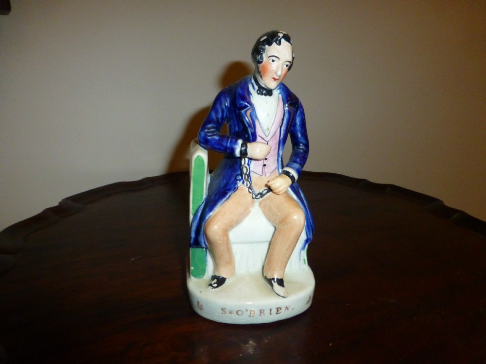 A Victorian Staffordshire earthenware portrait figure depicting Irish patriot William Smith OBrien seated in manacles, wearing a blue jacket and inscribed S. OBRIEN at the base.