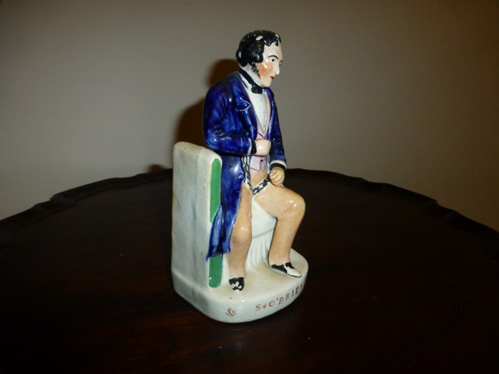 A Victorian Staffordshire earthenware portrait figure depicting Irish patriot William Smith OBrien seated in manacles, wearing a blue jacket and inscribed S. OBRIEN at the base. View II