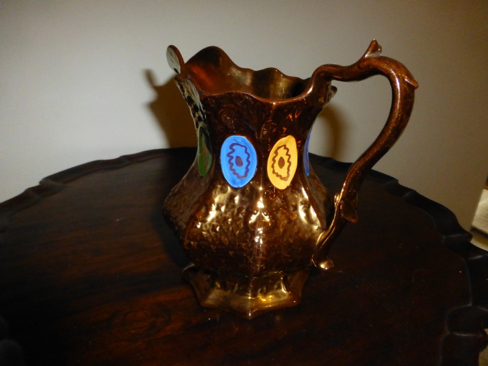 A Victorian copper lustre ceramic milk jug featuring a scalloped rim, scroll handle, and hand-painted enamel oval motifs in yellow, green, and blue. View II