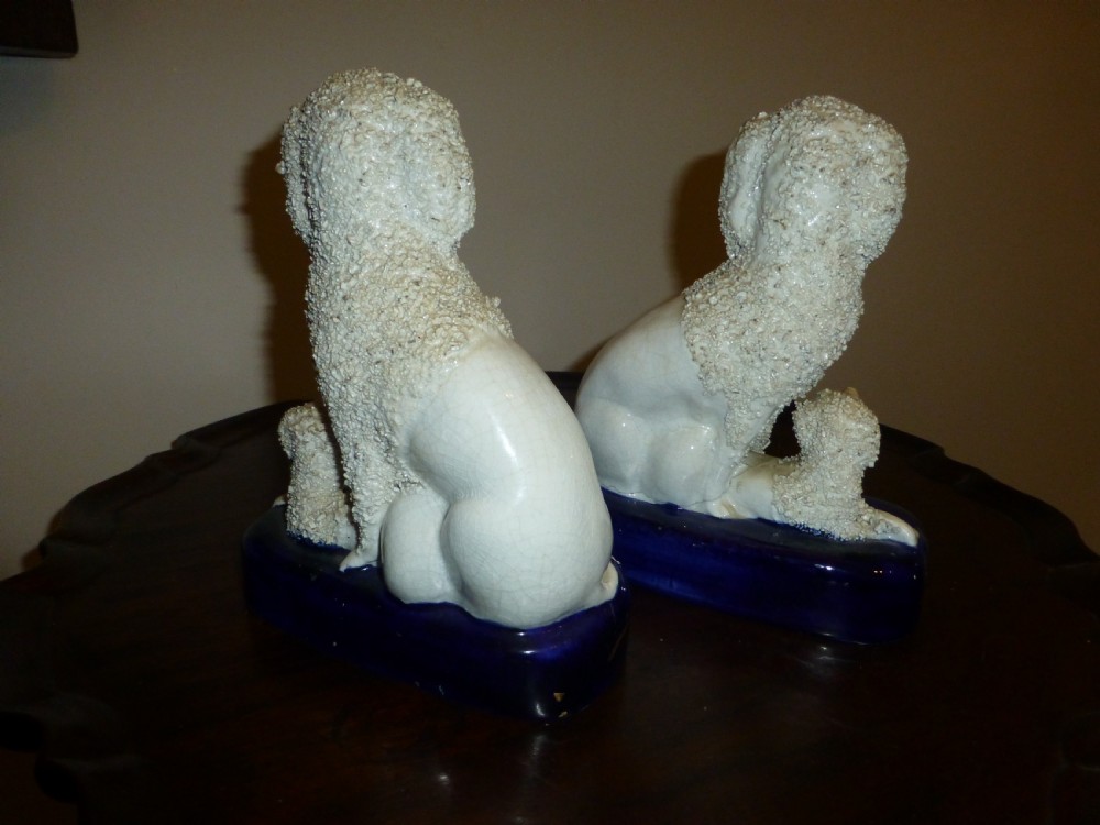 A pair of white textured Victorian Staffordshire ceramic poodles seated on cobalt blue bases with two small puppies beside each. View II