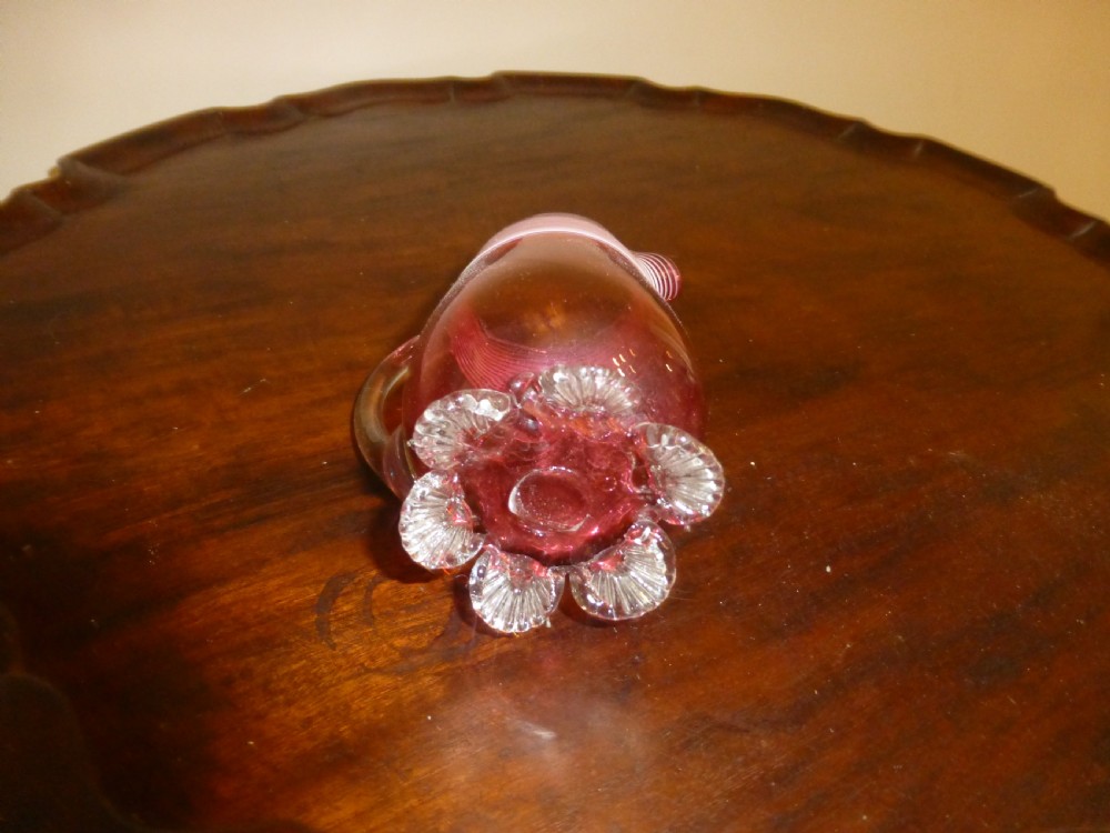 A Victorian cranberry glass cream jug featuring white threaded piping around the rim, a clear applied handle, and clear shell feet. View III