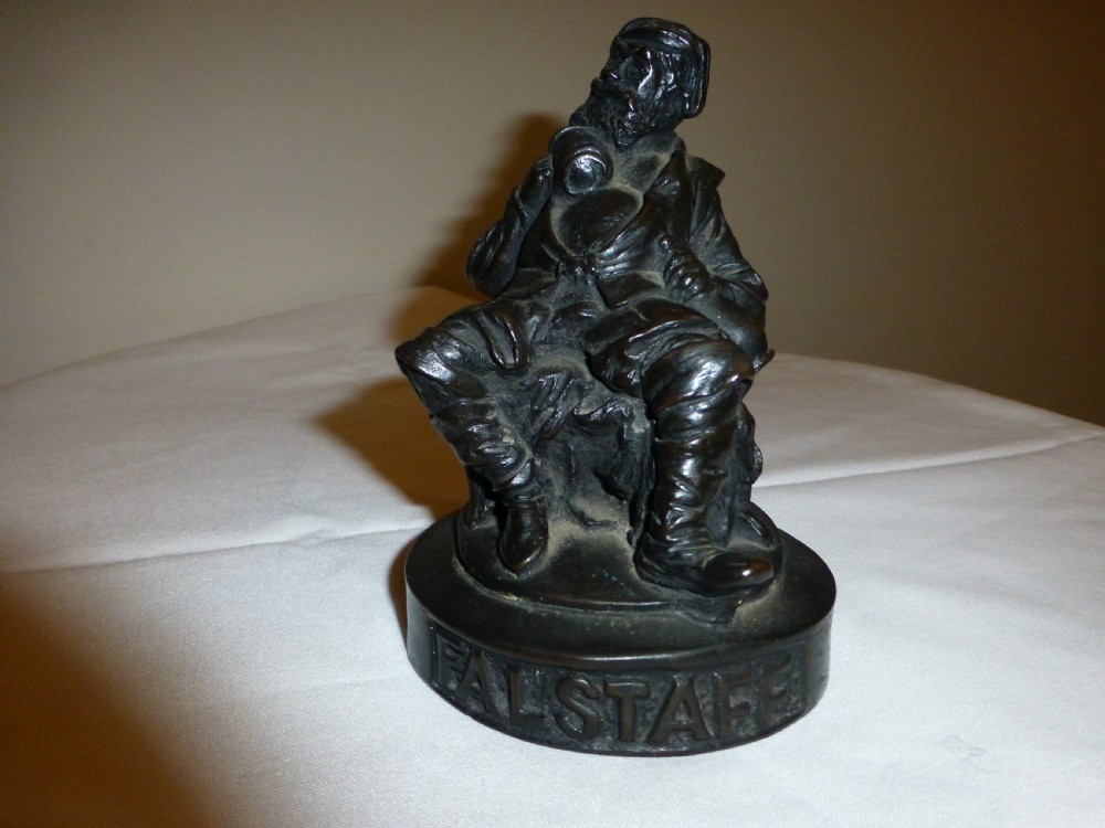 A late 19th-century dark bronzed metal figure depicting the seated Shakespearean character Falstaff on a round base with cast lettering.