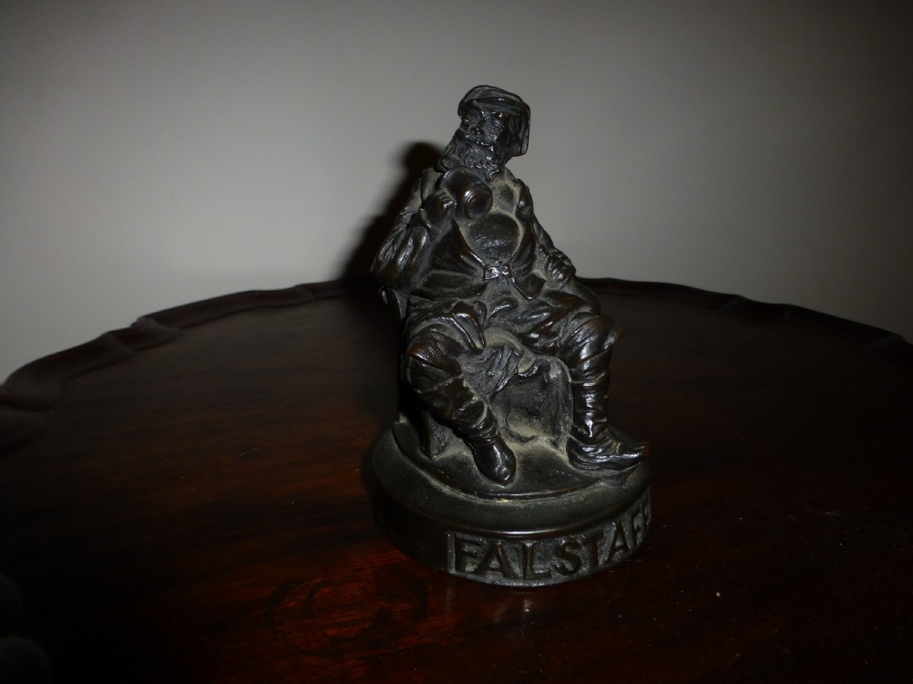 A late 19th-century dark bronzed metal figure depicting the seated Shakespearean character Falstaff on a round base with cast lettering. View II