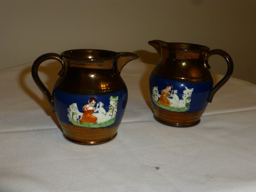 A pair of small ceramic cream jugs featuring metallic copper lustre glaze on the rims and bases with cobalt blue central bands showing hand-painted figures. View II