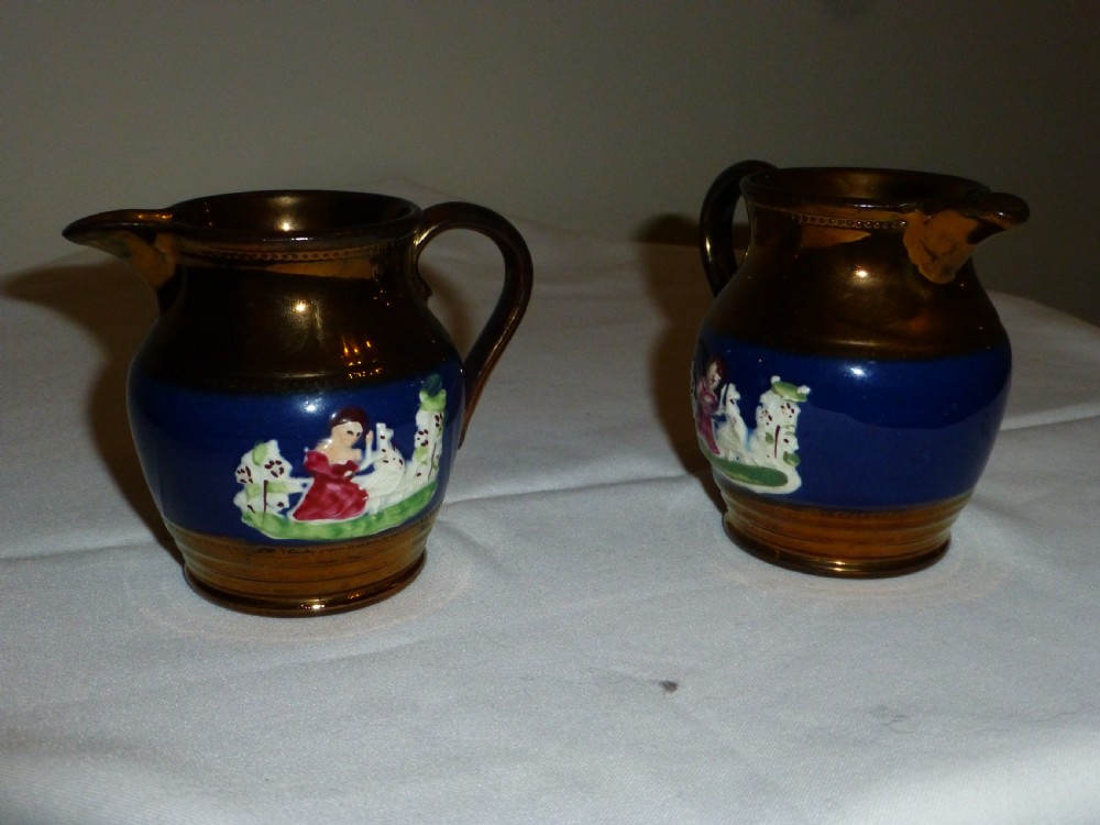A pair of small ceramic cream jugs featuring metallic copper lustre glaze on the rims and bases with cobalt blue central bands showing hand-painted figures. View III