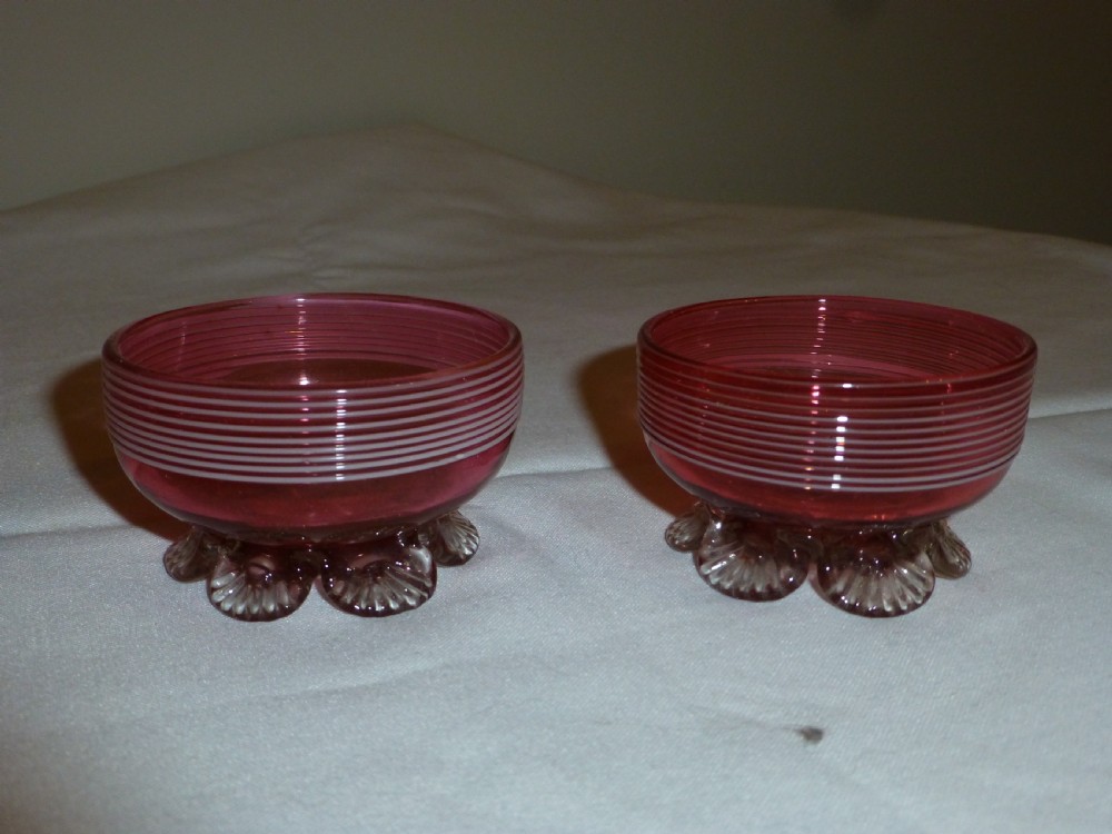 A pair of Victorian cranberry glass salt cellars featuring white horizontal glass trailing and shell-moulded feet.