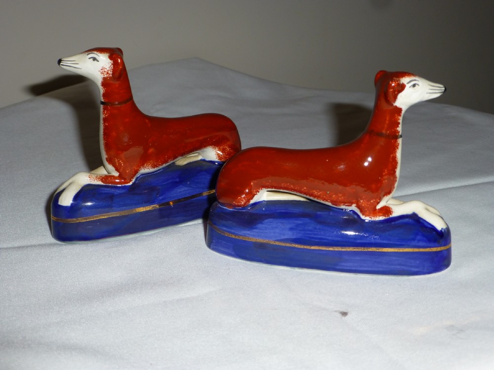 A pair of Victorian Staffordshire ceramic inkwells formed as reclining rust-red greyhounds set upon cobalt-blue glaze bases with gilded trim. View II
