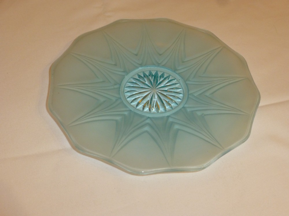A light blue frosted glass dish featuring a geometric starburst pattern radiating from a faceted central star motif.