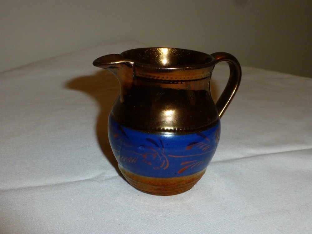 An antique Staffordshire ceramic cream jug with a metallic copper lustre body and a central bright blue band.