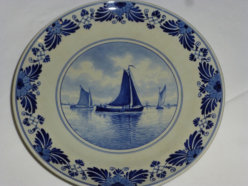 A circular 19th-century Delftware tin-glazed earthenware charger featuring a central hand-painted cobalt blue scene of sailing vessels on water surrounded by a floral rim pattern.