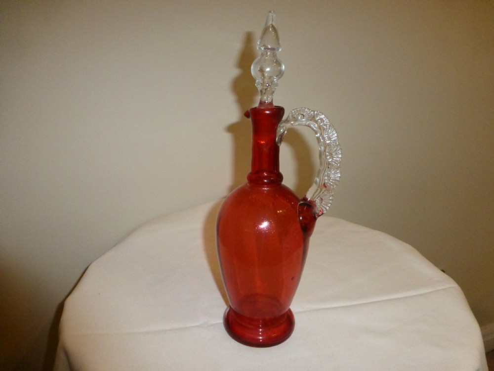A Victorian cranberry red glass decanter featuring a clear glass moulded handle and clear glass stopper.