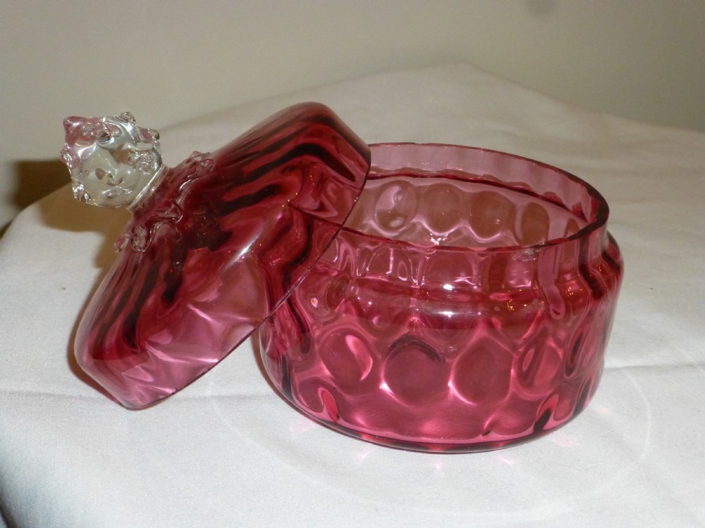 A circular Victorian cranberry glass lidded dish featuring a textured optic pattern and a clear glass finial top. View II