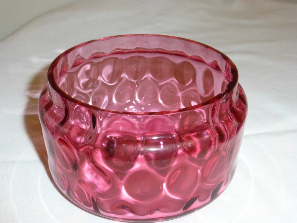 A circular Victorian cranberry glass lidded dish featuring a textured optic pattern and a clear glass finial top. View III