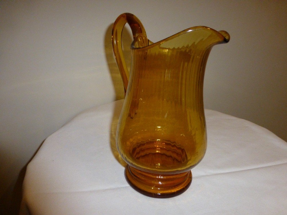 An amber glass lemonade jug featuring a ribbed body, an applied looped handle, a flared spout, and a solid circular base. View II