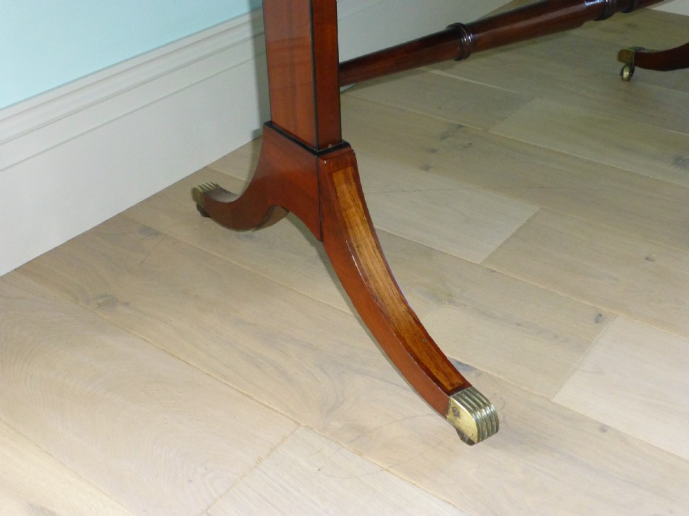 A Regency mahogany drop-leaf sofa table featuring two drawers with dark round knobs, splayed legs ending in brass castors, and a turned central stretcher. View VI
