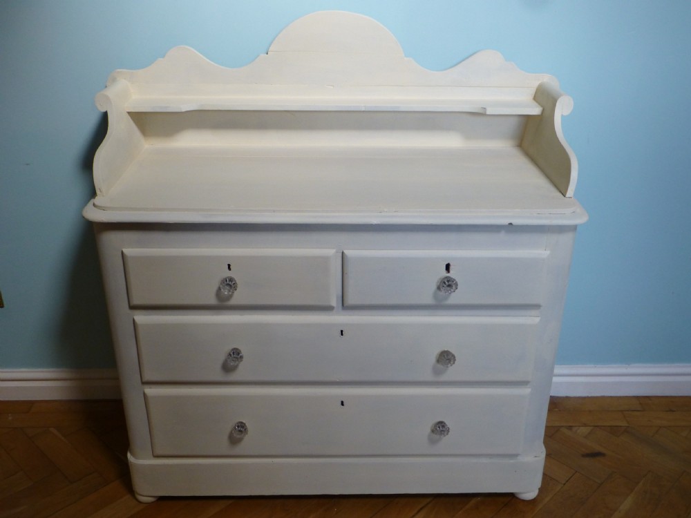 A cream-painted 19th-century Welsh pine chest of drawers featuring glass knobs and a shaped gallery upstand top shelf.
