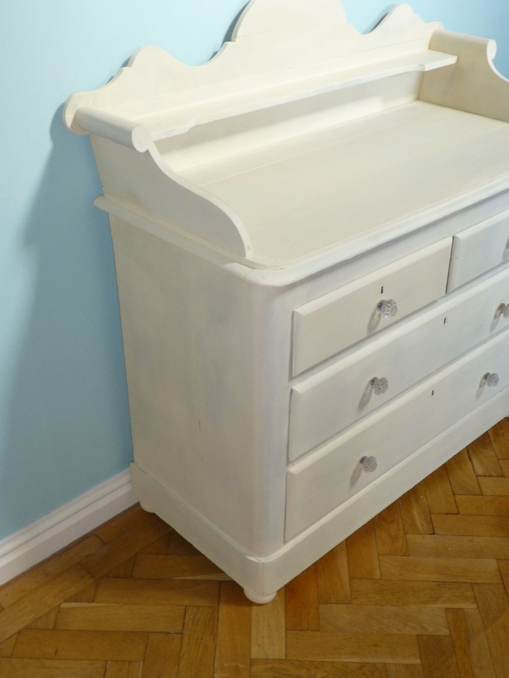A cream-painted 19th-century Welsh pine chest of drawers featuring glass knobs and a shaped gallery upstand top shelf. View II