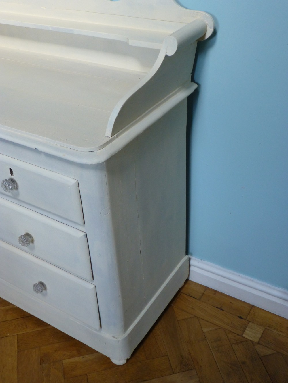 A cream-painted 19th-century Welsh pine chest of drawers featuring glass knobs and a shaped gallery upstand top shelf. View III