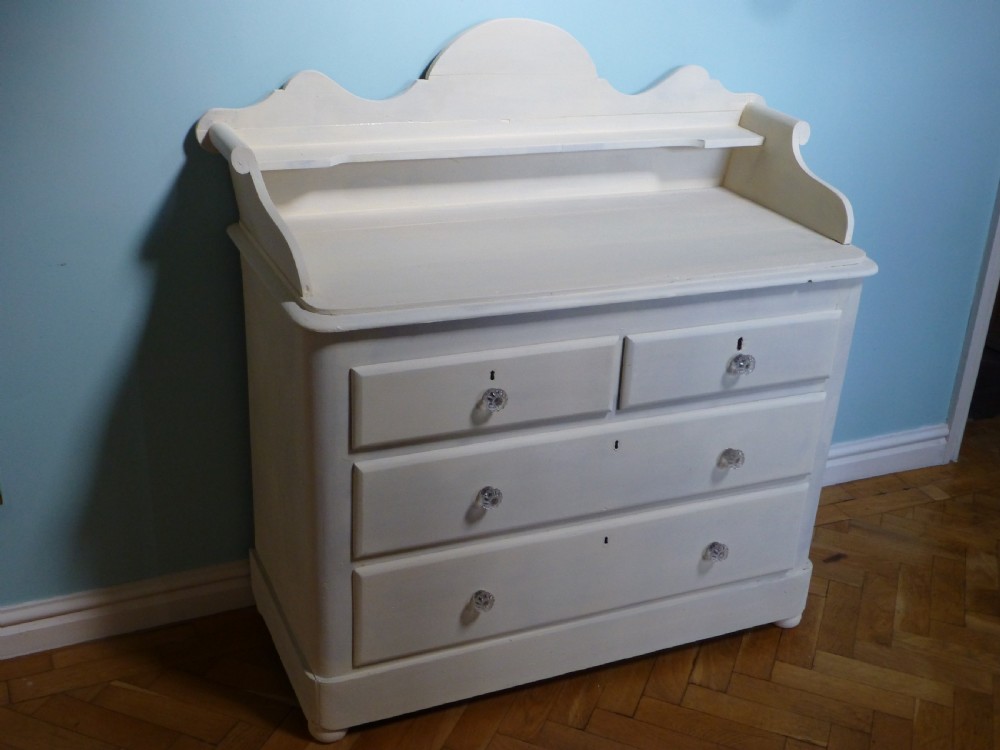 A cream-painted 19th-century Welsh pine chest of drawers featuring glass knobs and a shaped gallery upstand top shelf. View IV
