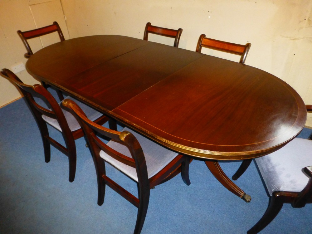 A Regency style mahogany extending dining table with twin pillar pedestal legs, surrounded by six matching mahogany chairs with light grey upholstered seats.