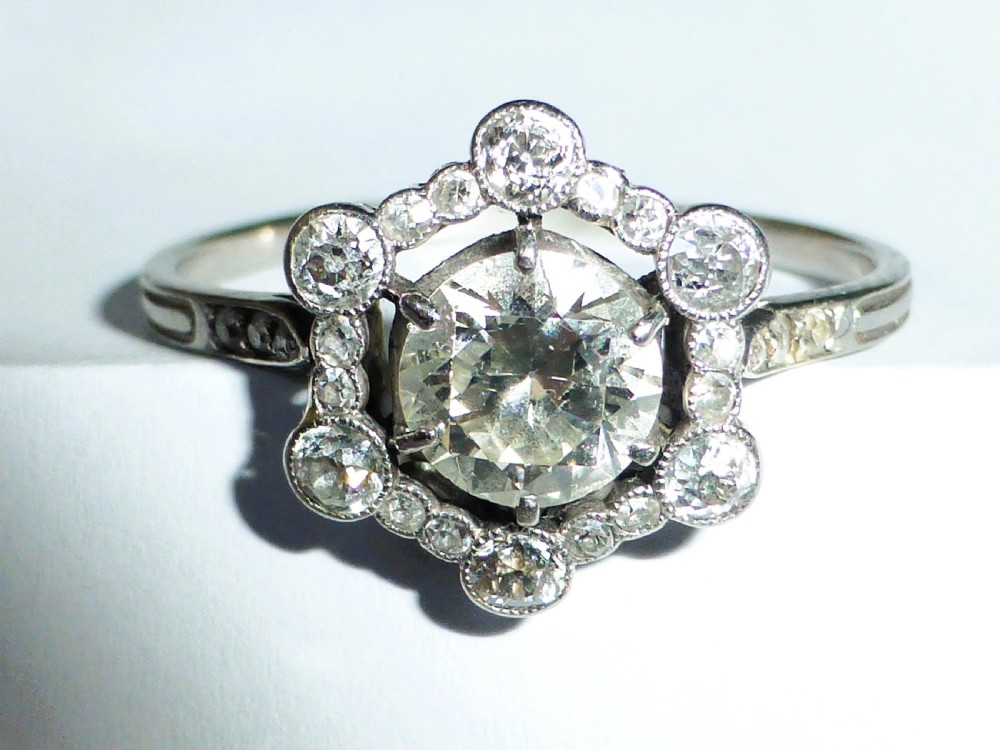 An Edwardian platinum ring featuring a central round diamond encircled by a hexagonal halo of smaller diamonds with milgrain borders.