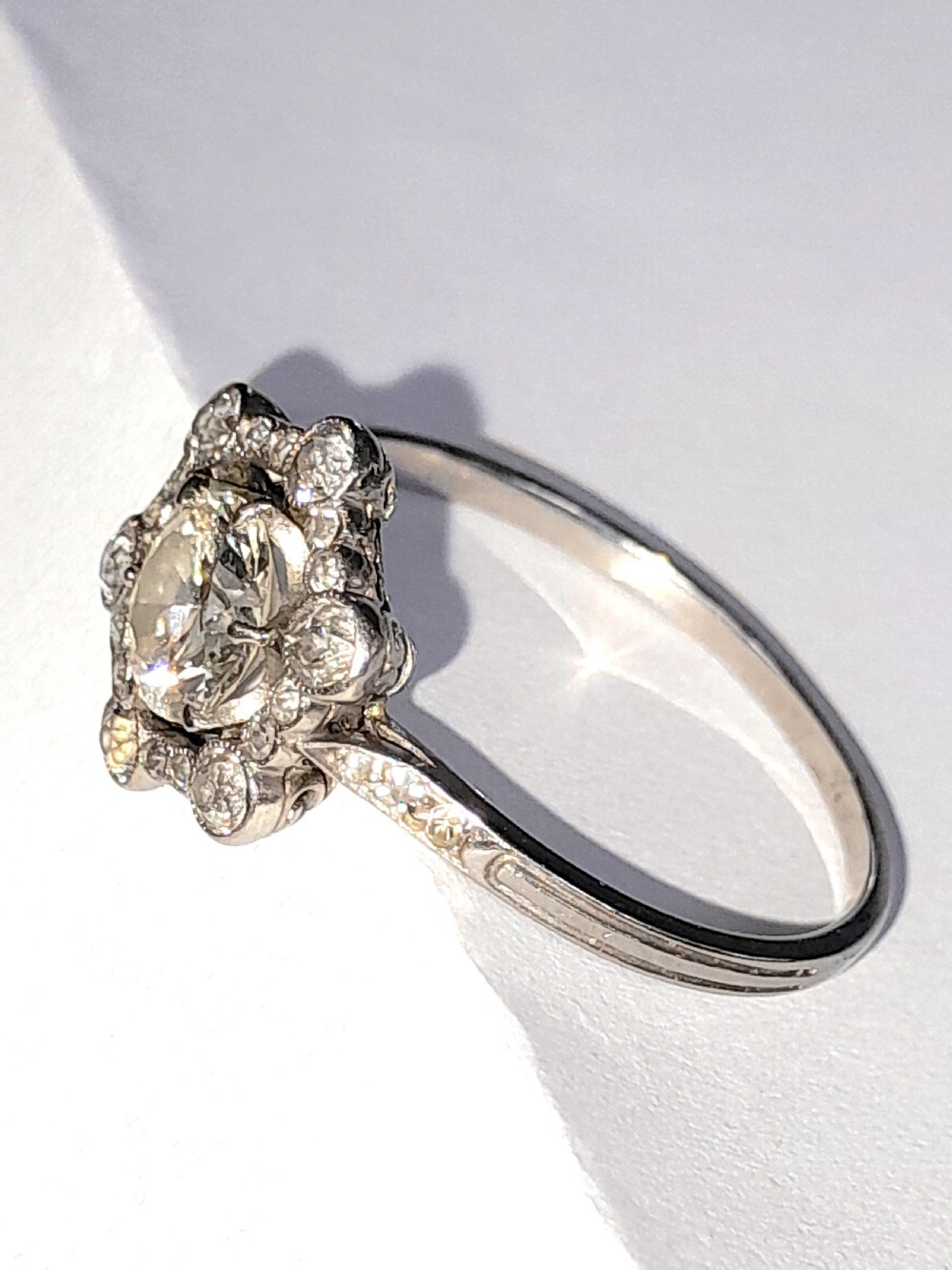 An Edwardian platinum ring featuring a central round diamond encircled by a hexagonal halo of smaller diamonds with milgrain borders. View III