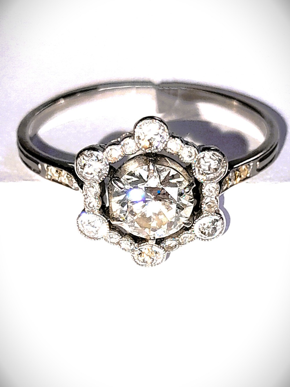 An Edwardian platinum ring featuring a central round diamond encircled by a hexagonal halo of smaller diamonds with milgrain borders. View IV