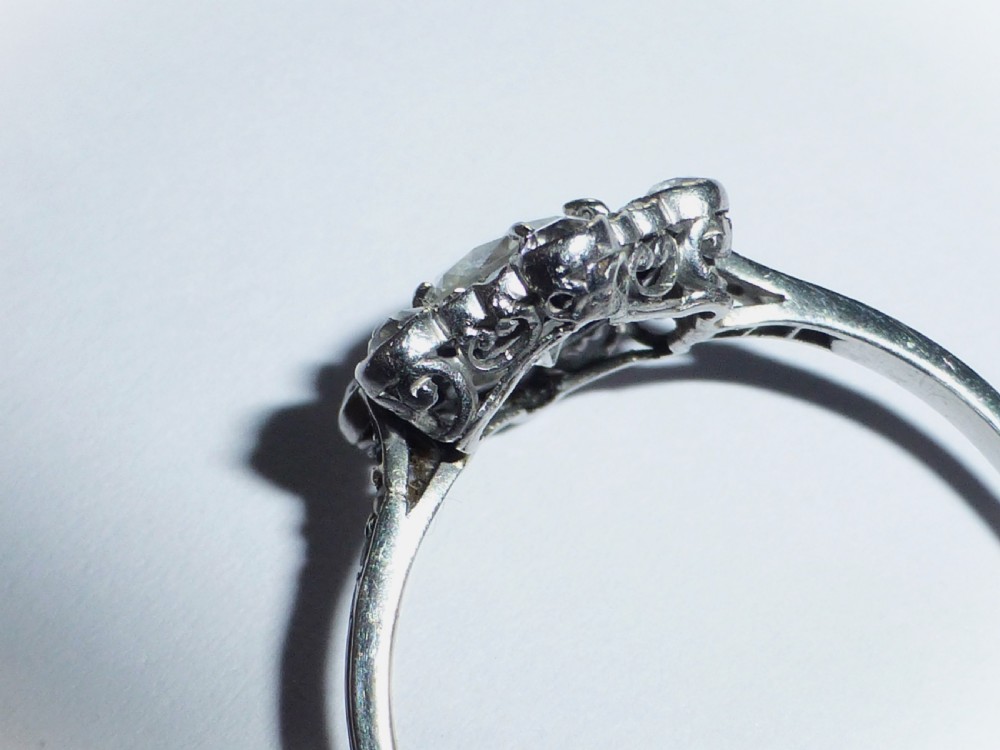An Edwardian platinum ring featuring a central round diamond encircled by a hexagonal halo of smaller diamonds with milgrain borders. View V