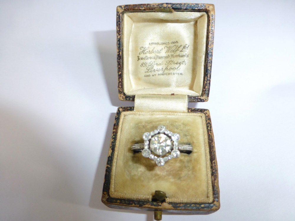An Edwardian platinum ring featuring a central round diamond encircled by a hexagonal halo of smaller diamonds with milgrain borders. View VI