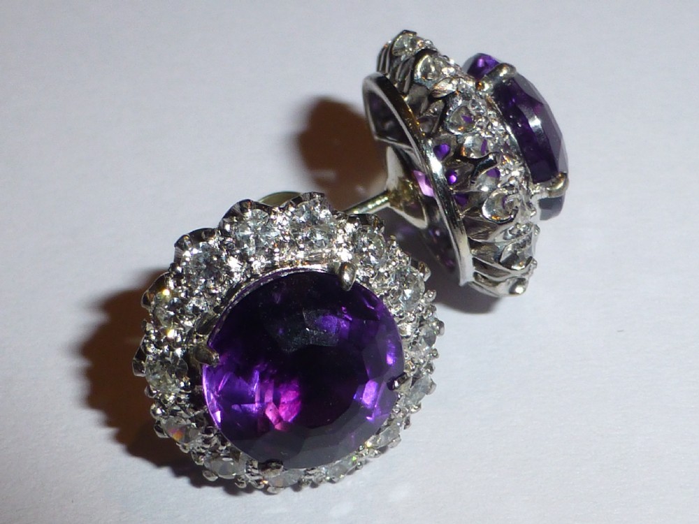A pair of round white gold stud earrings featuring central purple amethysts encircled by brilliant-cut diamonds.