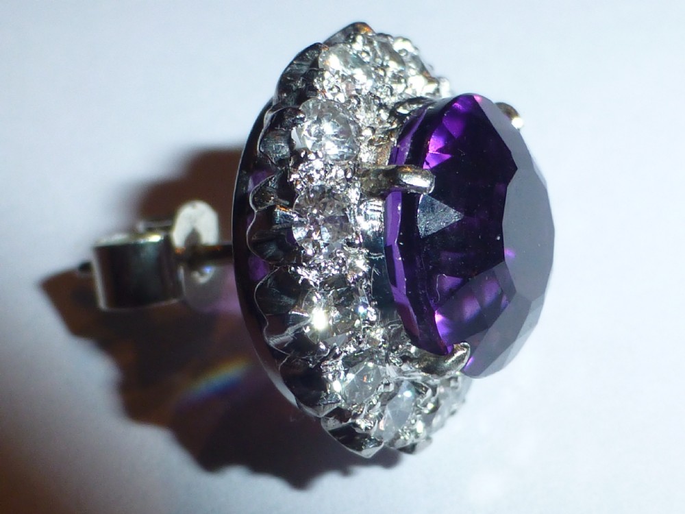 A pair of round white gold stud earrings featuring central purple amethysts encircled by brilliant-cut diamonds. View V