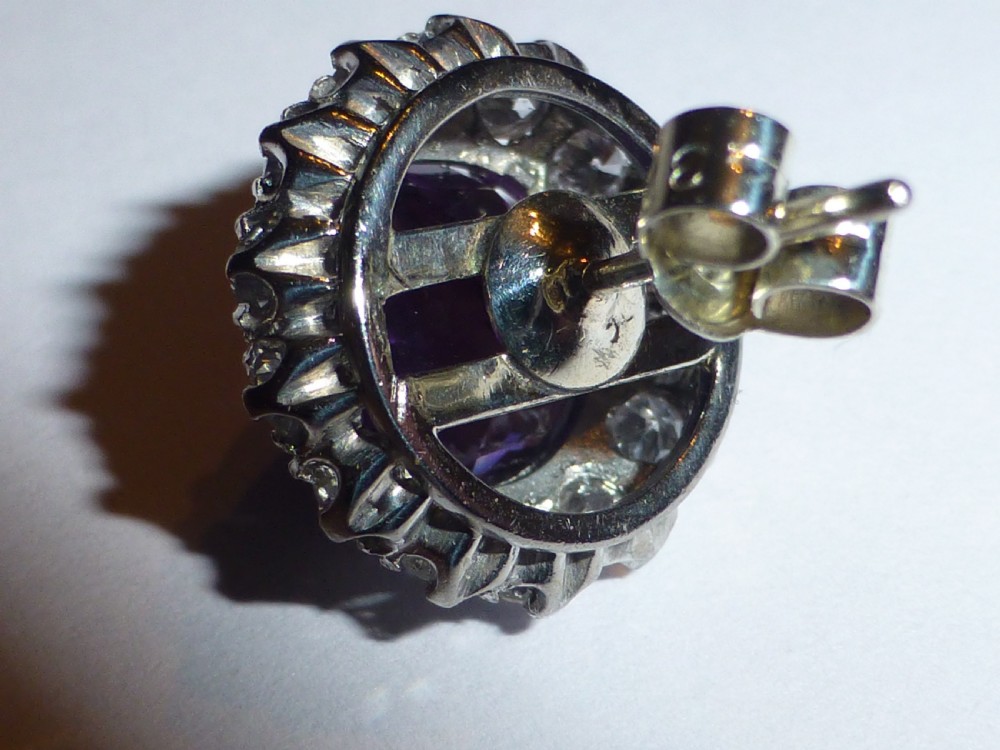 A pair of round white gold stud earrings featuring central purple amethysts encircled by brilliant-cut diamonds. View VI