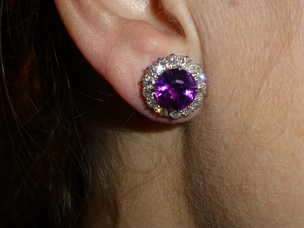 A pair of round white gold stud earrings featuring central purple amethysts encircled by brilliant-cut diamonds. View VII