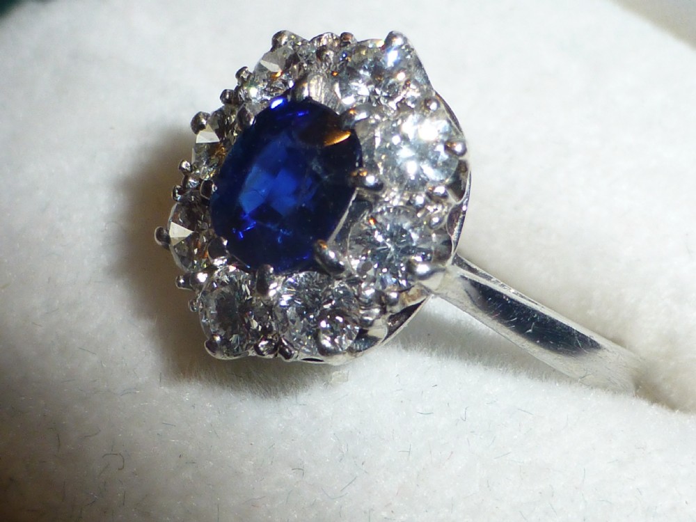 An Art Deco platinum cluster ring featuring a central oval blue sapphire surrounded by a halo of round diamonds.