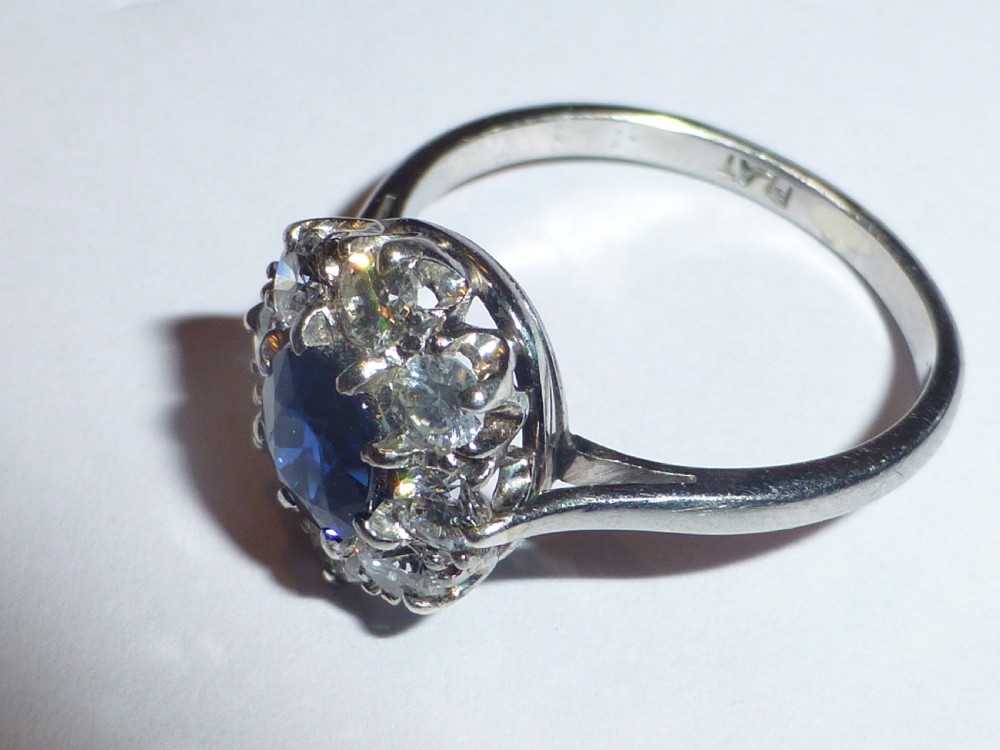 An Art Deco platinum cluster ring featuring a central oval blue sapphire surrounded by a halo of round diamonds. View III